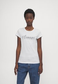 Witte katoenen T-shirt met korte mouwen, voorzien van een glanzend zwart "Armani Exchange" logo op de borst, gecombineerd met blauwe spijkerbroeken.