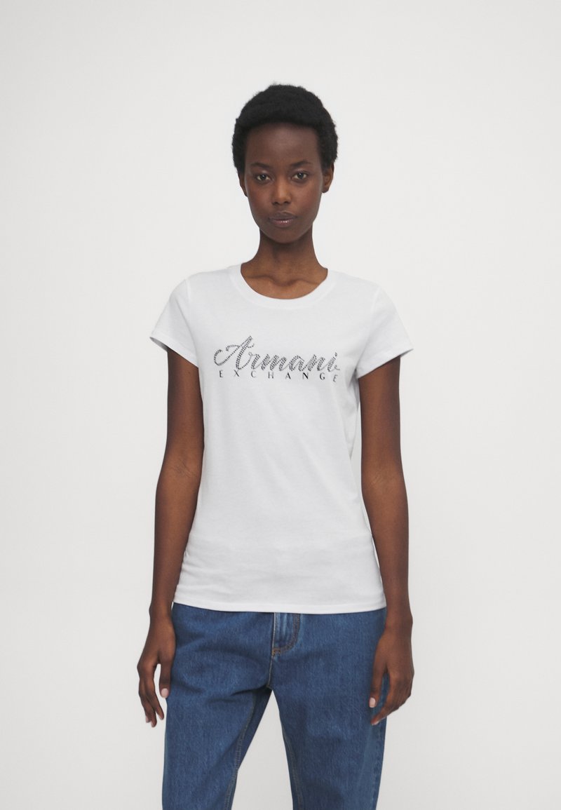 Witte katoenen T-shirt met korte mouwen, voorzien van een glanzend zwart "Armani Exchange" logo op de borst, gecombineerd met blauwe spijkerbroeken.