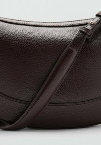Bolso de mano de cuero marrón oscuro con una superficie texturizada, forma curva y una larga correa ajustable. Presenta detalles de costura sutiles.