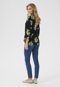 Blusa nera floreale con motivi verdi, maniche a tre quarti, vestibilità rilassata, abbinata a jeans skinny blu e ballerine beige chiare.