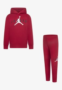 Sudadera roja con capucha y pantalones de chándal a juego, hechos de una tela suave. La sudadera cuenta con un bolsillo tipo canguro y un logo Jumpman blanco; los pantalones tienen una cinturilla elástica.
