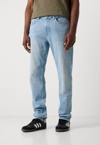 Light blue denim jeans with a straight-leg cut, five pockets, and a faded texture, paired with black sneakers featuring white stripes.
