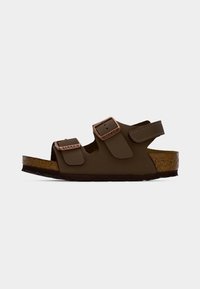 Καφέ ανοιχτό πέδιλο Birkenstock με δύο ρυθμιζόμενες αγκράφες και ιμάντα Velcro πάνω σε φελλό σόλα σε απλό φόντο.