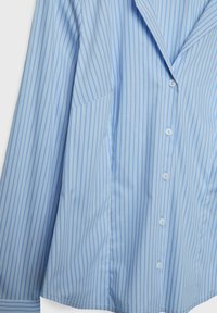 Camicia azzurra chiaro con strisce bianche verticali, dotata di colletto a V, chiusura con bottoni e una texture del tessuto liscia e morbida.