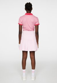 Kortärmad rosa polo med ett geometriskt mönster, ihop med en plisserad ljusrosa kjol. Vita strumpor med rosa detaljer och vita skor.