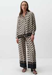 Gedrucktes zwei-teiliges Set aus seidigem Stoff mit einem Zickzackmuster in Beige, Schwarz und Braun. Locker sitzendes Hemd mit schwarzem Besatz und weit geschnittene Hose.