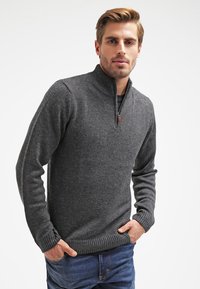 Suéter de punto gris con cuello con cremallera, puños acanalados y dobladillo. La textura es ligeramente texturizada, con un corte casual.