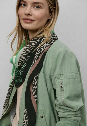 Green bomber jacket with a zip pocket, layered over a multicolored scarf featuring leopard print, stripes, and text accents.