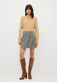 Beige neulepusero, harmaa ruudullinen mini-hame nappeilla ja ruskeat polvimittaiset saappaat. Suuri tekstuuri ja istuva malli.