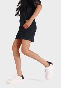 Sneakers bianchi con un accento nero nel tallone, texture liscia e punta rotonda. Indossati con un vestito di denim scuro, che mette in mostra uno stile casual.