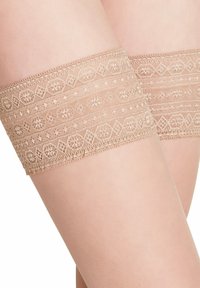 Calze color beige alti fino alla coscia con intricate rifiniture in pizzo che presentano motivi geometrici e dettagli raffinati lungo la fascia superiore. Texture liscia.