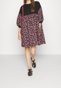 Czarna bluzka z bufkami i spódnica w kwiaty w odcieniach różu na ciemnym tle, w połączeniu z czarnymi sandałami na paseczkach.