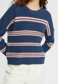 Granatowy sweter z dzianiny z poziomymi różowymi i ciemnoniebieskimi paskami, prążkowaną fakturą i okrągłym dekoltem. Casualowy fason.