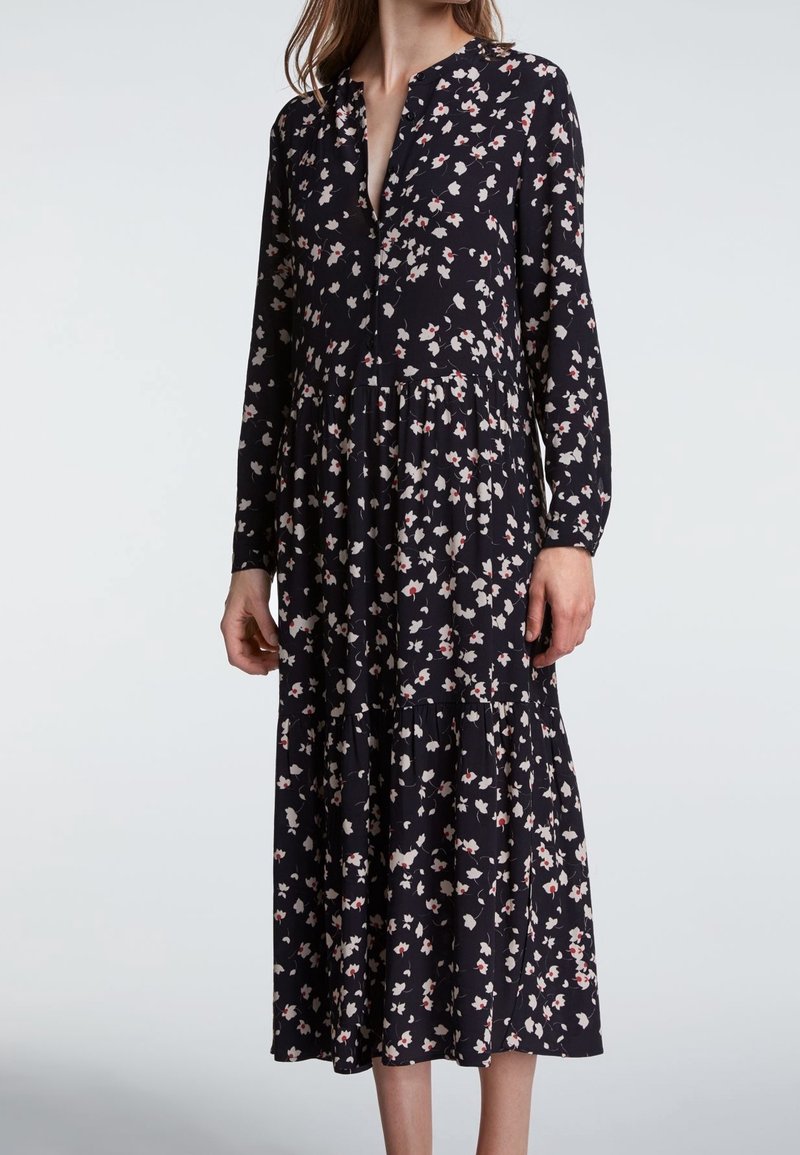 Kwiatowa sukienka na granatowym tle, z dekoltem w serek, długimi rękawami i warstwowym dołem. Całość zdobiona małymi różowymi i białymi wzorami kwiatowymi.
