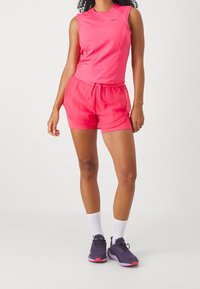 Top deportivo sin mangas de color rosa y pantalones cortos rosa a juego con un patrón texturizado, combinados con calcetas deportivas blancas y zapatillas moradas.