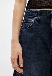 Tmavomodré rifľové nohavice s vysokým pásom, klasickým dizajnom s piatimi vreckami a striebornými kovovými doplnkami. Textúra je hladká s miernym vyblednutím.