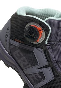 Grauer Wanderschuh aus Mesh-Material, mit bemerkenswertem BOA-Schnürsystem und einem gepolsterten Kragen. Verfügt über strukturierte Akzente und eine robuste Sohle.