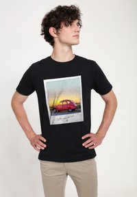 Svart t-shirt med en grafik av en vintage röd bil mot en solnedgång som bakgrund, med texten "Önskar att du var här!" nedan.