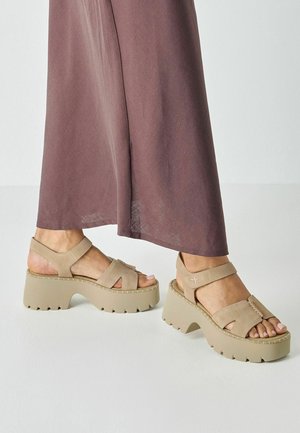 Beige platform-sandaler med åbne tæer, brede remme og tekstureret sål. Tykk, bølget hæl og dekorativ syningsdetalje på overdelen.