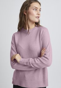 Lila stickad tröja med rund halsringning, långa ärmar och ribbade muddar och fåll. Tyget ser mjukt ut med en strukturerad yta.