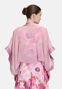 Lichtroze doorschijnende kimono met vloeiende mouwen, voorzien van bloempatronen op de achterkant. Satijnen accenten langs de randen verbeteren het ontwerp.