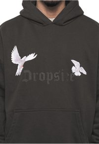 Sweat à capuche noir avec poche kangourou à l'avant, avec deux colombes blanches en vol et un texte sombre et discret "Dropsie" sur la poitrine.