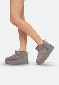 Botines grises hechos de un material similar al ante, con una gruesa plataforma, punta redondeada y una lengüeta en la parte trasera. Detalles texturizados en los laterales.