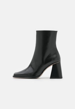 Zwarte leren enkellaars met een vierkante neus en een chunky, gestructureerde hak. Gladde oppervlak zonder zichtbare hardware of patronen.