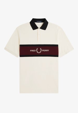 Short-sleeve beige polo shirt with black collar and horizontal maroon stripe featuring "Fred Perry" text and laurel logo across the chest.