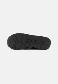 Suola di scarpa in gomma nera con un motivo testurizzato, caratterizzata da più scanalature per il battistrada e un logo circolare vicino al tallone.
