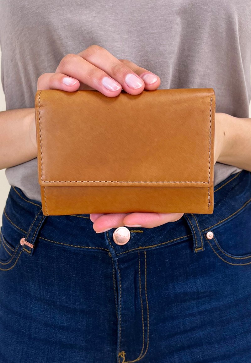 Tan leather wallet with a rectangular shape, featuring visible stitching and a smooth texture, held in hands against a gray shirt background.