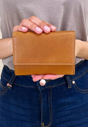 Tan leather wallet with a simple design, rectangular shape, exposed stitching, and a fold-over closure, held in a hand.