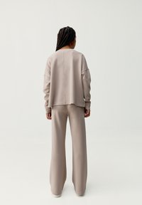 Beige, oversized sweatshirt a široké kalhoty z jemné, hladké tkaniny. Obsahuje spadlé ramena a minimalistický design. Žádné viditelné logo.