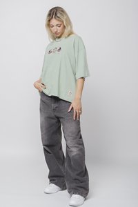 Tricou oversized de culoare verde deschis cu imprimeu grafic, asortat cu blugi largi gri estompați și adidași albi. Confortabil, cu un croi lejer.