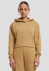 Sudadera con capucha recortada en beige, hecha de una tela suave. Presenta mangas largas con puños de canalé y una banda ancha en el dobladillo.