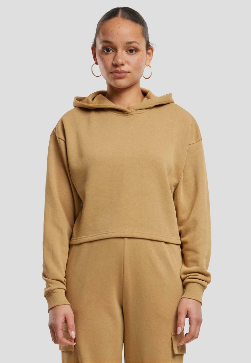 Sudadera con capucha recortada en beige, hecha de una tela suave. Presenta mangas largas con puños de canalé y una banda ancha en el dobladillo.