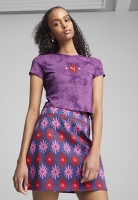 Fioletowa koszulka cropped w wzór tie-dye z czerwonym haftem, połączona z granatową spódnicą w różowe i czerwone kwiatowe wzory.