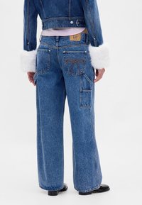 Wijde blauwe spijkerbroek met een achterzakje met een striksteekdetail en een GAP-label. De stof heeft een klassieke versleten textuur.