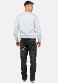 Felpa grigia abbinata a jeans neri con cuciture decorative, diverse tasche e un design unico della tasca posteriore. Look informale.