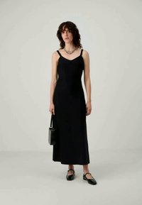 Μαύρο αμάνικο μάξι φόρεμα με εφαρμοστό κορσέ, ρευστή φούστα και διακριτική γυαλάδα. Συνδυασμένο με μαύρες φλατ και μια μικρή τσάντα.