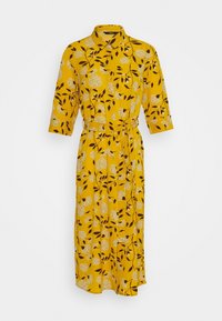 Gul blommig klänning med trekvartslånga ärmar, ett bälte i midjan och en krage. Har ett blad- och blommönster i mörkbrunt och vitt.