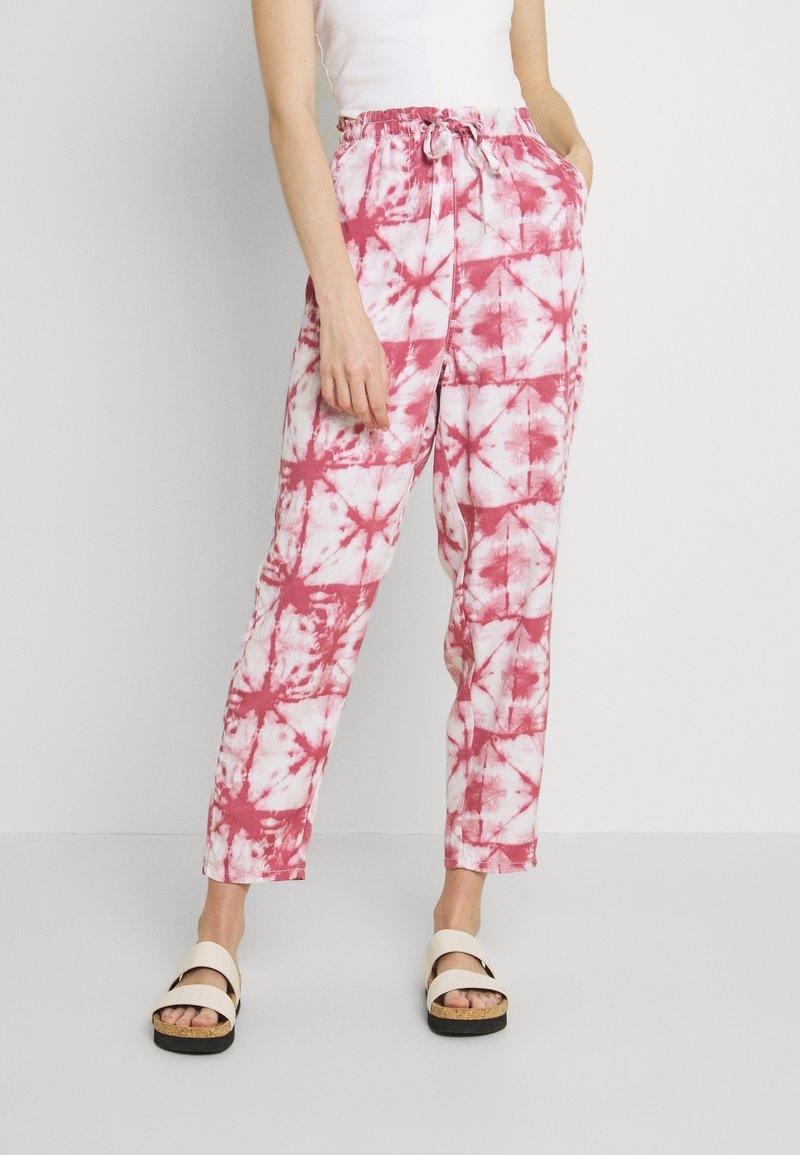 Personne portant un pantalon ample tie-dye rose et blanc avec une taille élastique et des sandales blanches à semelles en liège.