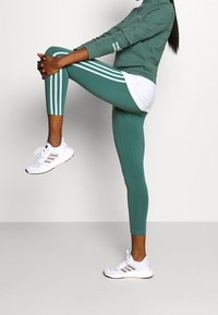 Conjunto de ropa deportiva en turquesa que incluye leggings ajustados con rayas blancas, una camiseta de manga larga a juego y zapatillas deportivas blancas con detalles en gris.