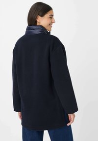 Cappotto in pile blu navy con collo imbottito, vestibilità oversize e maniche lunghe. Tessuto morbido con taglio dritto, adatto per un abbigliamento casual.