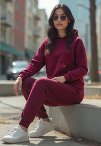 Burgundowy sweatshirt z kapturem i dopasowane spodnie wykonane z miękkiego materiału, z kieszenią z przodu i ściagaczami, w połączeniu z białymi sneakersami.