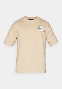 Camiseta de algodón beige con mangas cortas, con un gráfico floral y la letra "A" en la parte izquierda del pecho. Textura suave y ajuste clásico.
