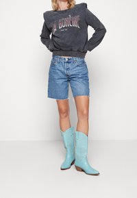 Szara bluza z napisem „LA BOHÈME”, niebieskie dżinsowe szorty oraz turkusowe kowbojki z misternym haftem i spiczastymi czubkami.