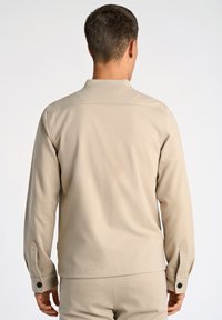 Beige långärmad skjorta med krage, med knäppte manschetter och rak höft. Slät tyg med en subtil textur och inga synliga mönster.