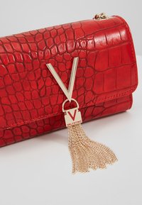 Borsa a tracolla in ecopelle di coccodrillo rossa con dettaglio hardware a forma di V in tonalità oro e frangia a catena. Design compatto e strutturato.