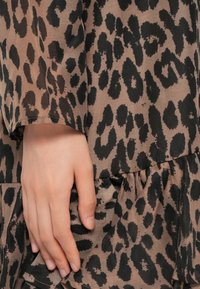 Main reposant contre un tissu avec un motif léopard marron et noir sur un vêtement.